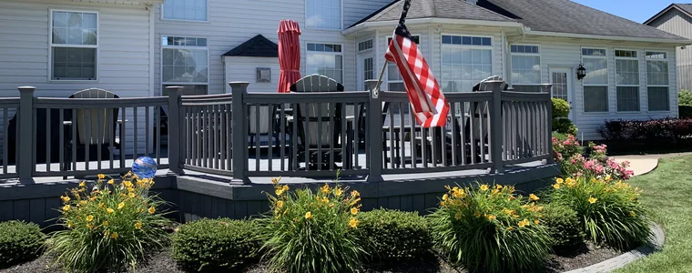 A large grey composite deck and railing at a white two-storey home, cleaned by Bronny's Power Washing.