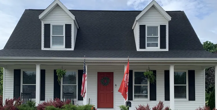 A white two-storey home with black shutters and a red front door, cleaned by Bronny's Power Washing.