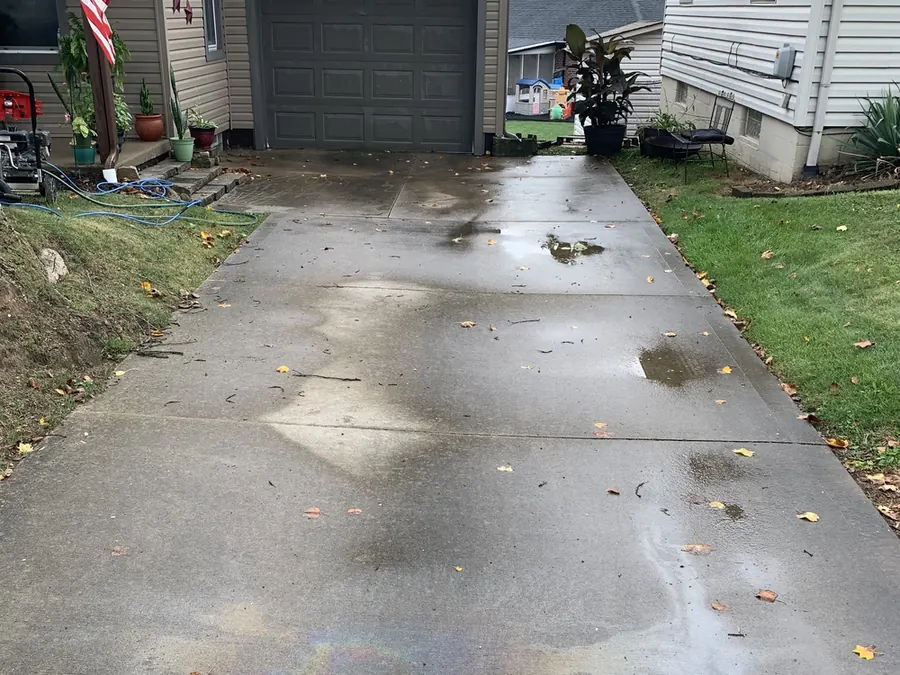 A concrete driveway before cleaning, darkened by algae, dirt and an oil stain.