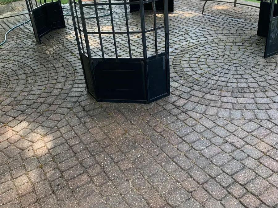 A brick paver patio under a gazebo before cleaning, grey-green with moss between the pavers.
