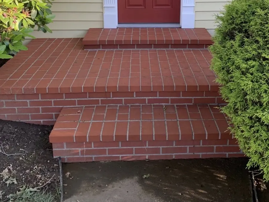 The same brick porch and steps after pressure washing by Bronny's Power Washing, with the brick and mortar cleaned back to their original red colour.