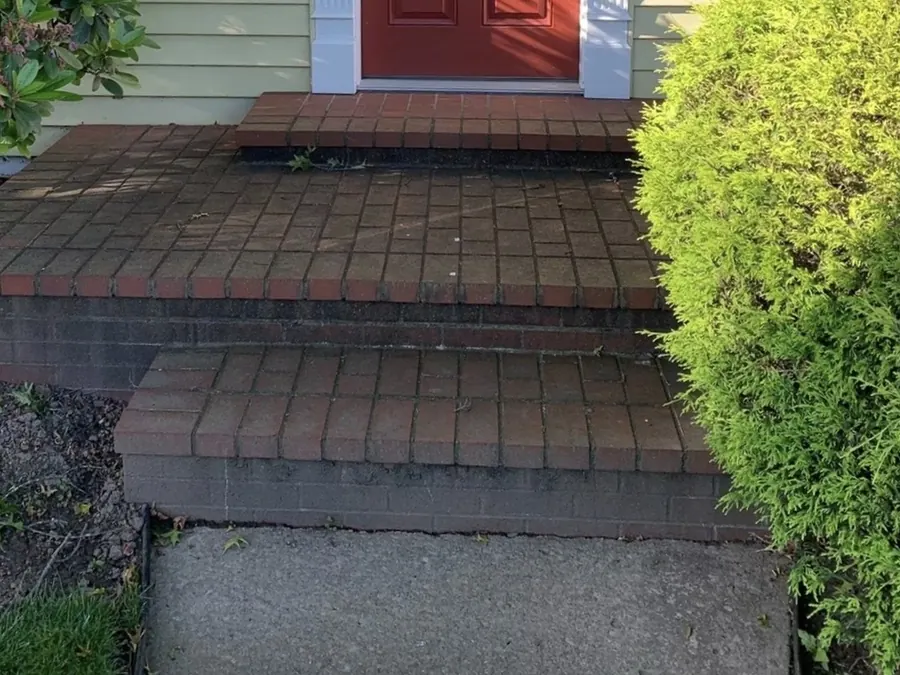 Brick front porch and steps before pressure washing, darkened by ground-in dirt, moss and algae.